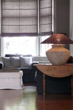 a living room filled with furniture and a lamp on top of a wooden table in front of a window