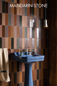 a blue pedestal sink sitting next to a wall covered in brown and tan tiles with the words mandarin stone on it