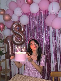 a woman holding a cake with candles in front of balloons