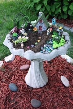 a birdbath filled with lots of plants and small houses on top of it