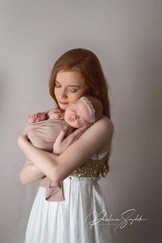 a woman in a white dress holding a newborn girl with her arms wrapped around her