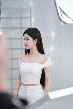 a woman with long hair standing in front of a mirror wearing a white top and skirt