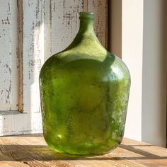 a green glass bottle sitting on top of a wooden table next to a window sill