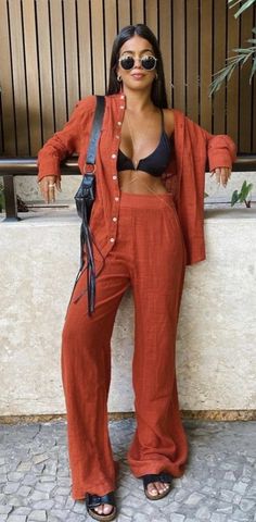 a woman standing next to a wall wearing an orange jumpsuit and black bra top