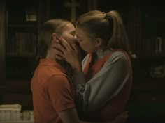 two women are kissing each other in front of a book shelf and bookshelf