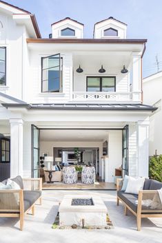 a large white house with lots of windows and furniture on the front porch, facing an outdoor fire pit