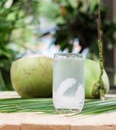 a glass filled with water sitting on top of a wooden table next to coconuts