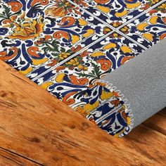 an orange, blue and yellow floral pattern on wood flooring with grey fabric covering it