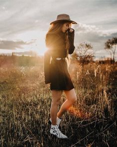 a woman wearing a hat standing in the middle of a field with her hands behind her head