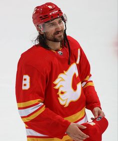 a man with long hair wearing a red and yellow jersey on the ice in front of an arena