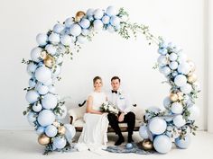 a bride and groom sitting on a bench in front of an arch decorated with balloons