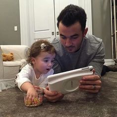 a man is holding a child while looking at an electronic device on the floor in front of him