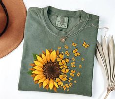 a green t - shirt with a sunflower on it next to a straw hat