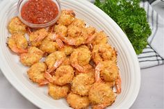 a white plate topped with fried shrimp next to a small bowl of sauce and parsley