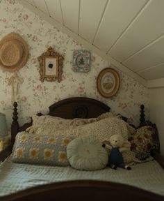 a bed with pillows and stuffed animals on it in a room that has floral wallpaper