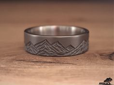 a wedding band with mountains engraved on the side is sitting on a wooden table top