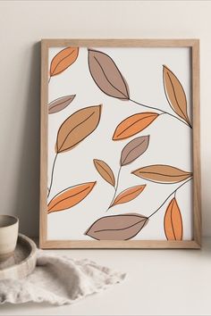 an orange and brown leaf print on a white wall next to a cup with a saucer