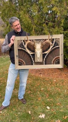 a man holding up a painting with an animal's head on it in the grass