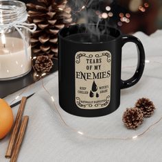 a black coffee mug sitting on top of a table next to candles and pine cones