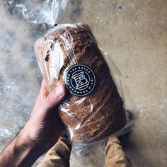 a person holding a loaf of bread wrapped in plastic on top of a cement floor