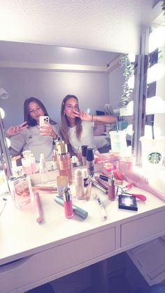 two women taking pictures of themselves in a mirror with makeup products on the counter top