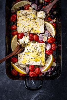 fish with tomatoes, onions and lemons in a cast iron skillet on a dark surface