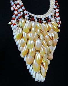 Indonesian Irian braided beige Rope triangular front necklace, decorated with oval curled golden Mother-of-Pearl Shells,beneath bunched red and white Job Tear's seeds. At the top of the triangular front are three rows of combination of seeds , and around the rim are white Cowrie Shells. The largest mother of Pearl shells, are each, approximately, 1.75 inches in length, and the smallest are 1 inch in length. The maximum width of the necklace is 7 inches, and the drop length, at the triangular fro Beige Teardrop Bohemian Jewelry, Bohemian Beige Teardrop Jewelry, Beige Bohemian Teardrop Jewelry, Bohemian Shell Cream Jewelry, Traditional Handmade Beige Jewelry, Traditional Handmade Cream Necklace, Traditional Cream Handmade Necklace, Bohemian Cream Shell Jewelry, Bohemian Style Cream Shell Jewelry