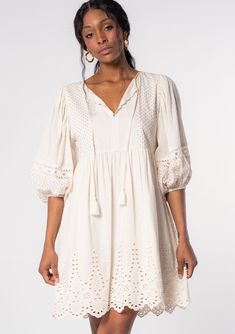 Classic bohemian details and effortless Summer style come together in this timeless cotton mini dress. Designed in a textured dobby and a contrast mini red dot print, featuring a flowy embroidered skirt, a split v-neckline with tassel tie accents, and voluminous long sleeves with sheer lace trim. An essential warm-weather style that pairs effortlessly with a lace-up sandal. FINAL SALE Dobby and dot print Embroidered Relaxed, flowy fit Voluminous long sleeve Elastic wrist cuff Split v-neckline wi Flowy Cotton Boho Dress With V-neck, Spring V-neck Peasant Dress, Flowy V-neck Peasant Dress, Spring Peasant V-neck Dress, White Peasant V-neck Dress, Flowy V-neck Peasant Boho Dress, Bohemian Midi Dress With Broderie Anglaise, Bohemian Short Sleeve Broderie Anglaise Dress, Chic V-neck Dresses With Broderie Anglaise