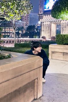 a person leaning against a wall in front of a cityscape with buildings and trees