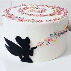 a white cake decorated with sprinkles and a silhouette of a fairy