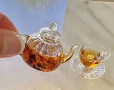 a hand is holding a glass tea pot and cup