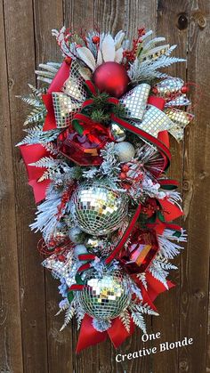 a christmas wreath hanging on the side of a wooden fence with red and silver decorations