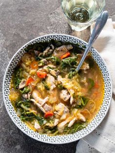 a bowl of chicken and vegetable soup next to a glass of water