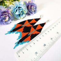 an orange and black beaded earrings sitting on top of a ruler next to flowers