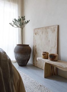 a bedroom with a bed, table and vase on the floor in front of a window