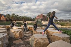 a girl jumping off rocks into the air with other people in the background looking on