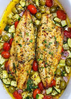 two fish fillets in a white bowl with tomatoes, cucumbers and olives