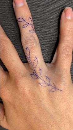 a person's hand with a small tattoo on their left thumb and the middle finger