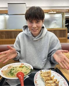 a young man sitting at a table with two plates of food in front of him