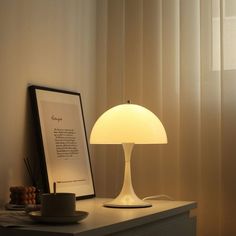 a table lamp sitting on top of a white dresser next to a framed photograph and cup