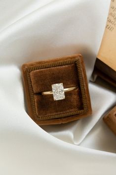 an engagement ring in a velvet box on top of a white cloth with a book behind it