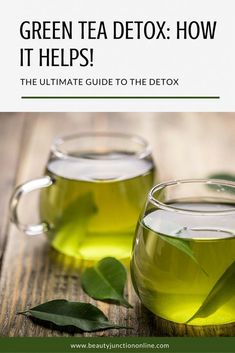 two mugs filled with green tea sitting on top of a wooden table next to leaves