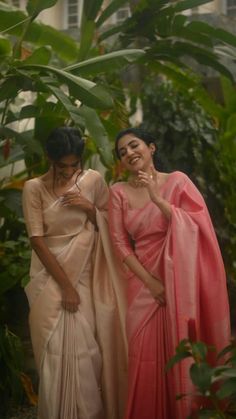 two women standing next to each other in front of plants