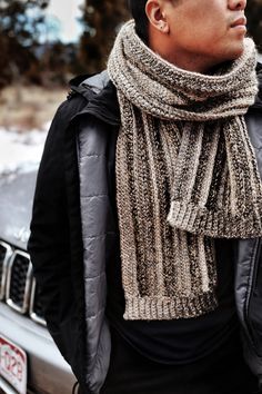 a man standing in front of a car wearing a knitted scarf over his neck