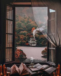 an open book sitting on top of a wooden table next to a window filled with candles