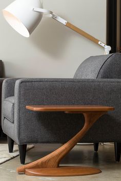 a grey couch with a wooden table in front of it and a white lamp on the side