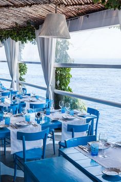 an outdoor dining area overlooking the ocean with blue and white table cloths, place settings and chairs