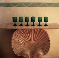 a table with green glasses on it and a shell shaped shelf over the top that holds five wine glasses