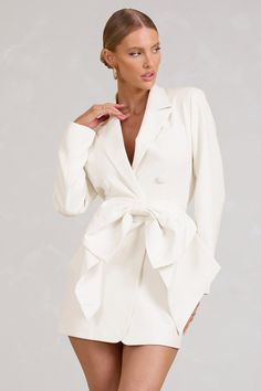 a woman is wearing a white suit with a tie around the waist and short shorts