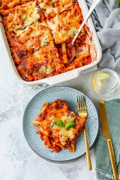 a casserole dish with meat and cheese on it next to a fork, glass of water and silverware